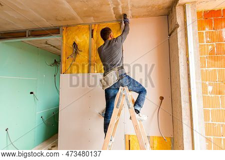 Repairman On Wooden Ladder Holds Professional Manual Power Tool Acu Drill And Tightens The Screws On