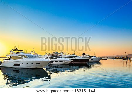 Luxury yachts docked in sea port at sunset. Marine parking of modern motor boats and blue water. Tranquility, relaxation and fashionable vacation.