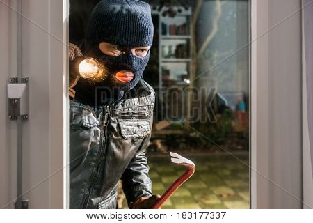 Burglar With Flashlight And Crowbar Looking Into Glass Window