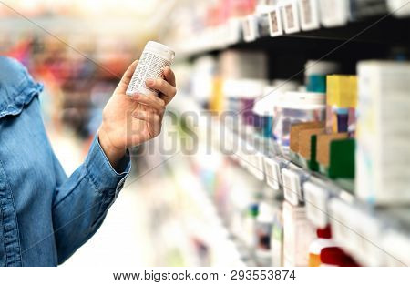 Customer In Pharmacy Holding Medicine Bottle. Woman Reading The Label Text About Medical Information