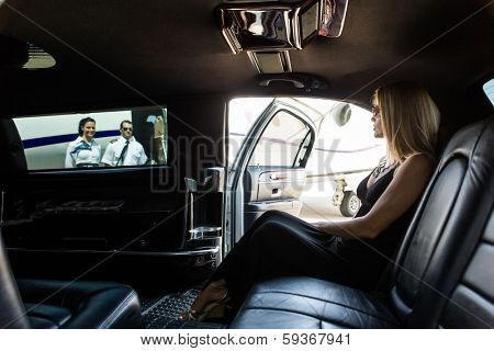 Elegant woman in limousine with airhostess and pilot near private jet at terminal