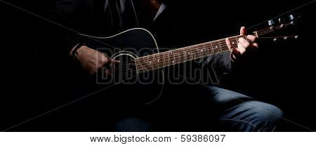 Young musician playing acoustic guitar and singing, on dark background