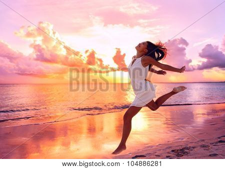 Happy beautiful free woman running on the beach at sunset jumping playful having fun in serene picturesque sunset at the ocean . Aspirational happy lifestyle with pretty young lady enjoying freedom.