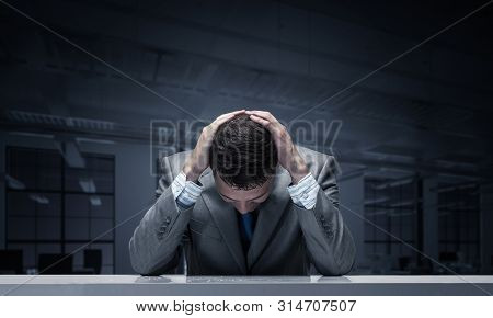 Frustrated Man Sitting At Desk With Hands On Head. Businessman Stressed From Pressure At Work. Unemp