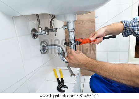 Male Plumber Fixing Sink In Bathroom