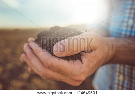 Farmer holding pile of arable soil male agronomist examining quality of fertile agricultural land close up with selective focus