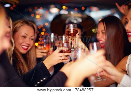 Beautiful Women Clinking Glasses In Limousine. Focus On Glasses