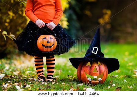 Little girl in witch costume playing in autumn park. Child having fun at Halloween trick or treat. Kids trick or treating. Toddler kid with jack-o-lantern. Children with candy bucket in fall forest.