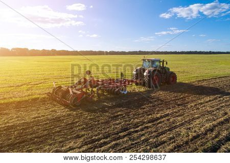 Agricultural tractor plowing the field at sunset. Agricultural machinery in field