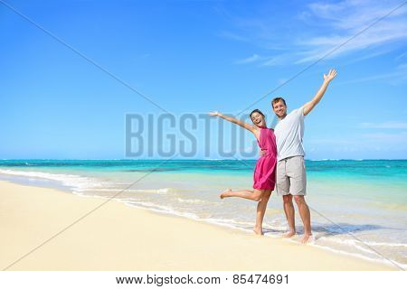 Freedom on beach vacation - happy carefree winning couple with arms up showing happiness and fun on paradise beach with perfect pristine turquoise water in sunny tropical getaway