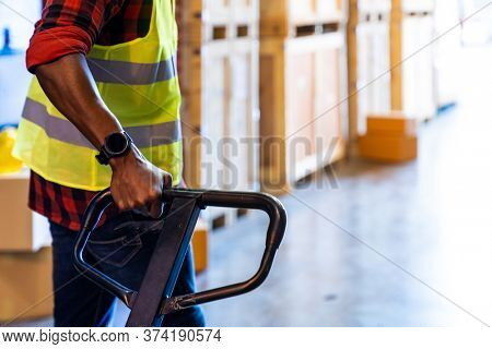 Close up of african black warehouse worker hand hold hand pallet jack in distribution warehouse with copyspace. Business warehouse and logistic concept.