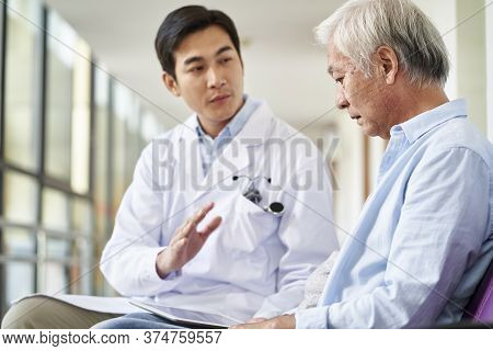 Young Asian Doctor Talking And Explaining Test Result And Diagnosis To Demoralized Elderly Patient I