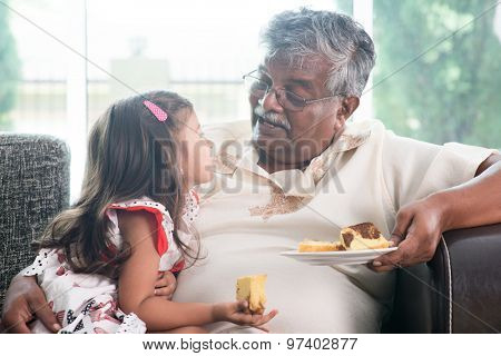 Portrait of Indian family at home. Grandparent and grandchild eating butter cake. Asian people living lifestyle. Grandfather and granddaughter.