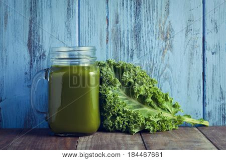 a kale smoothie served in a glass mason jar and a leaf of kale on a wooden surface against a blue rustic wooden background