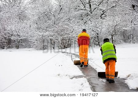 Unrecognizable workers removing first snow from pavement in park