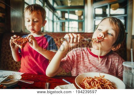 kids eat pizza and pasta at cafe. children eating unhealthy food indoors