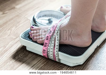 Feet tied up with measuring tape to a weight scale. Addiction and obsession to weight loss. Anorexia and eating disorder concept.