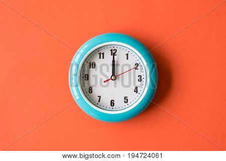 Blue wall clock on orange background twelve o'clock