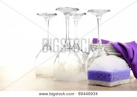 Dishes in foam with gloves and wisp on table isolated on white