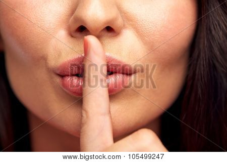 silence, gesture and beauty concept - close up of young woman holding finger on lips