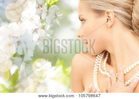 beauty, luxury, people, holidays and jewelry concept - beautiful woman with sea pearl necklace or beads over cherry blossom background