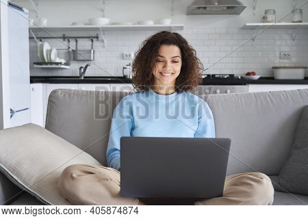 Happy Hispanic Teen Girl Holding Laptop Computer Device Technology Sitting On Couch At Home. Smiling