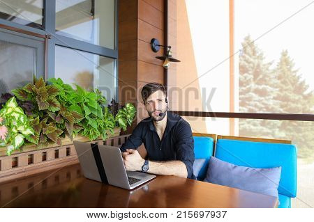 Educational consultant talking to student by laptop video call with headset microphone. Handsome serious man has beard and wears black shirt. Concept of assisting students in making decisions and giving advices in tuition fees, visa, and enrolling at High