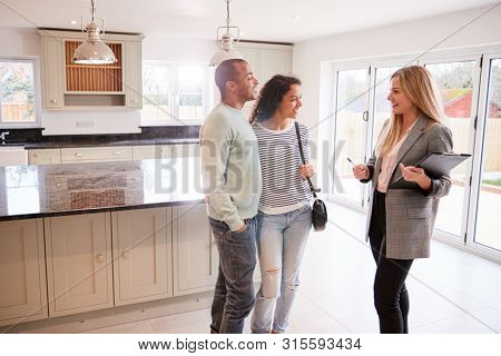 Female Realtor Showing Couple Interested In Buying Around House