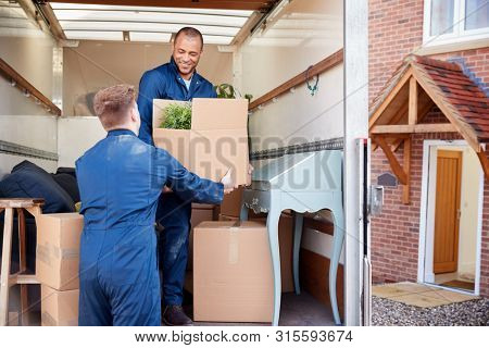 Removal Company Workers Unloading Furniture And Boxes From Truck Into New Home On Moving Day