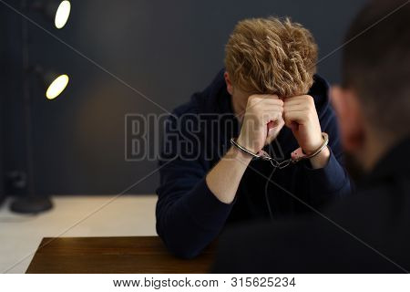 Police Officer Interrogating Criminal In Handcuffs At Desk Indoors, Space For Text