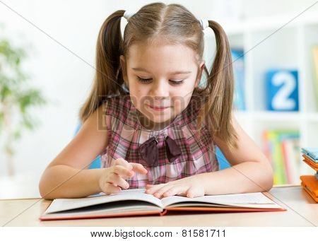 Cute kid girl reading story from big book in nursery