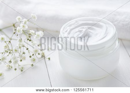 Anti wrinkle anti-aging cosmetic cream skincare and face care moisture lotion with herbal flowers in glass jar with towel on white background