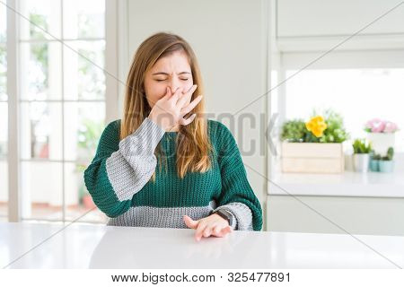 Young beautiful plus size woman wearing casual striped sweater smelling something stinky and disgusting, intolerable smell, holding breath with fingers on nose. Bad smells concept.