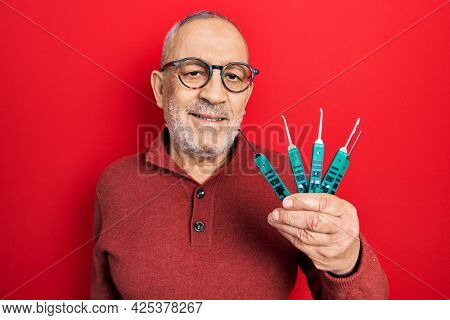 Handsome mature man holding picklock to unlock security door looking positive and happy standing and smiling with a confident smile showing teeth 