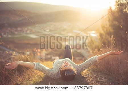 Carefree happy woman lying on green grass meadow on top of mountain edge cliff enjoying sun on her face.Enjoying nature sunset.Freedom.Enjoyment.Relaxing in mountains at sunrise.Sunshine.Daydreaming