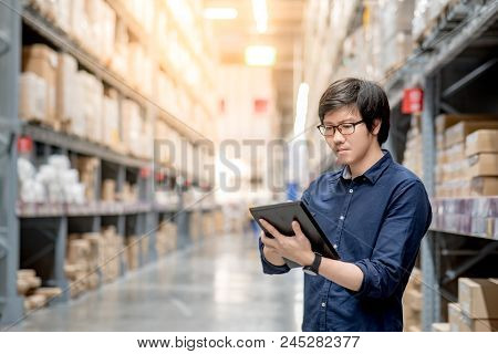 Young Asian Man Doing Stocktaking Of Product In Cardboard Box On Shelves In Warehouse By Using Digit