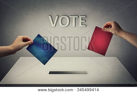 Election Concept As Two People Hands Holds Different Color Ballot Papers At The Polling Station. You