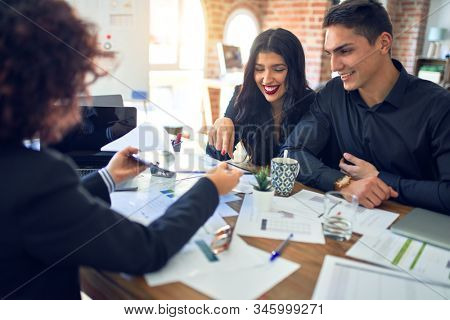 Young beautiful couple applying for mortgage. Sitting smiling happy meeting with real state agent considering mortgage loan at bank