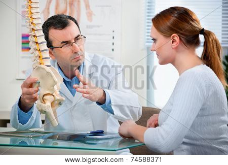 Physical Therapist shows the problem areas on the model of the spine to patient and explains the cause of her pain.