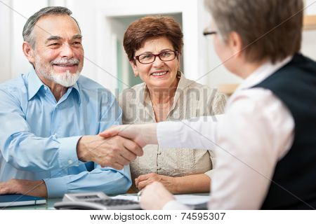 senior couple smiling while shaking hand with financial advisor