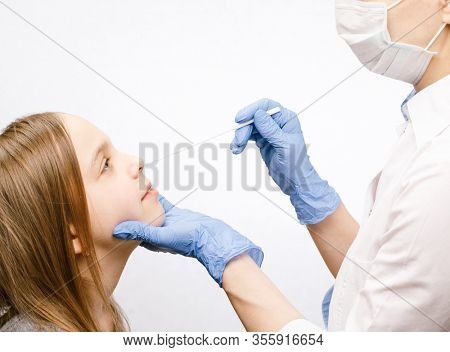 Pediatrician or doctor taking nasal mucus test sample from elementary age girl's nose performing respiratory virus testing procedure