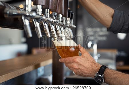 Hand of bartender pouring a large lager beer in tap. Closeup of hand serving beer in glass using tap. Close up of barman hand at beer tap pouring an amber draught beer at pub.