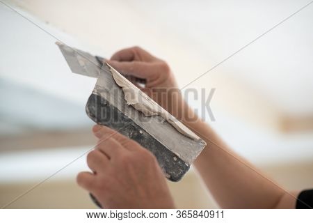 Worker putsty plasterboard ceiling in new building. Repairman works with plasterboard, plastering dry-stone wall, home improvement. A man makes repairs at home. Putty knife in male hand