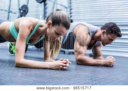 Side view of a muscular couple doing planking exercises