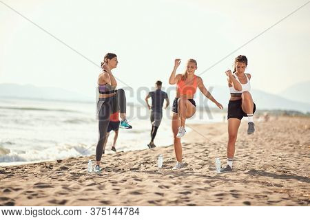 group of three women exercise on a sandy beach with two men jogging in the background