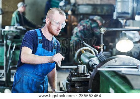 worker turner operating lathe machine at industrial manufacturing factory