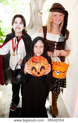 Üç çocuk hile ya da kapıda tedavi Halloween kostümleri.  Önünde küçük bir çocuk üzerinde odaklanmak