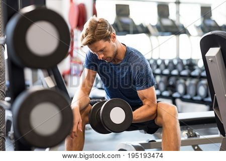 Young handsome man training at a fitness center. Fit guy lifting dumbbell at gym. Portrait of a young muscular man exercising with dumbbells in the gym.