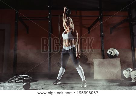 Fitness woman doing a weight training by lifting kettlebell. Muscular fitness woman, holds up a black kettlebell in the gym. Fitness woman in the gym. Fitness woman.