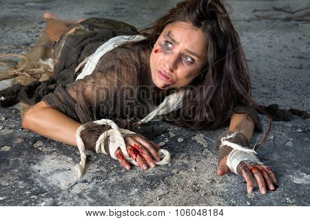 Young abused and frightened woman sitting on the floor of a derelict building